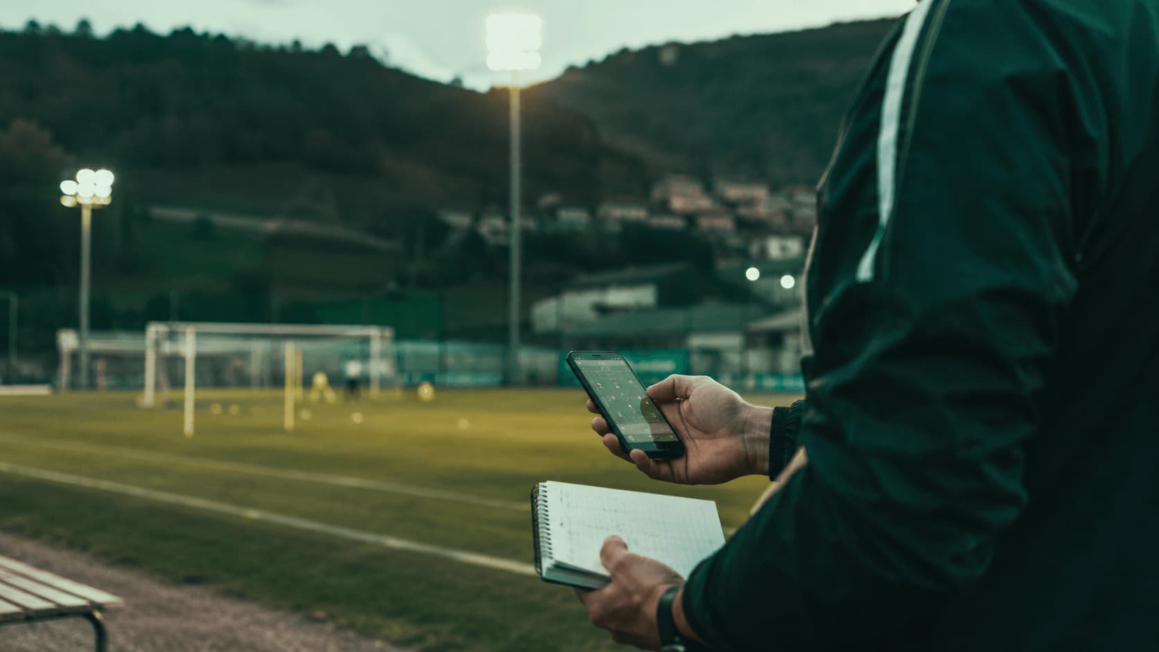 Allenatore guarda i dati della rosa sul telefono a bordo campo dopo l'allenamento